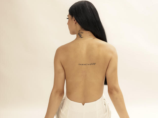 StormeAss ha lunghi capelli neri, un tatuaggio sul collo ed è senza top, indossando pantaloni bianchi, mostrando la schiena. Ha dei seni piccoli e un sedere slanciato e attraente..