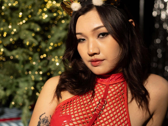 ShadowStrike has a cute face with Asian features, wearing a red fishnet top, gold cat ears, and a strap, showing a tattoo on her arm, with pouty lips.