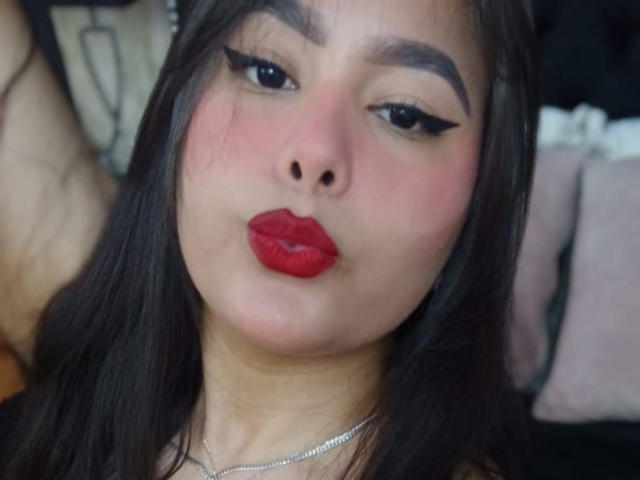 BrianaRogers has red lipstick, black eyeliner, and a slightly flushed face with dark brown hair, looking directly at the camera with a pouty expression.