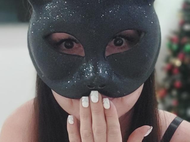 NewCrystal with a dark, glittery mask covering her eyes, her white-manicured fingers in front of her mouth, black hair, and a black strap visible on her shoulder.