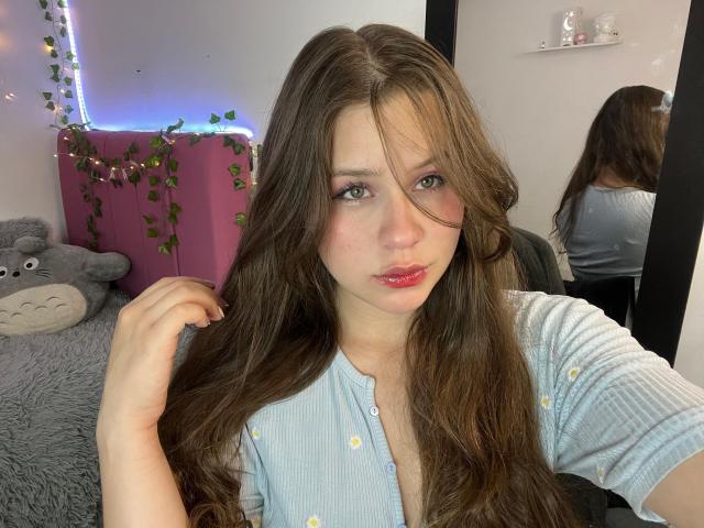 SwanKyivy met lang bruin haar, volle roze lippen, een lichtblauwe geribbelde top, haar vasthoudend, spiegelbeeld, een grijze pluchen kat, een paarse doos met wijnranken, zachte verlichting..