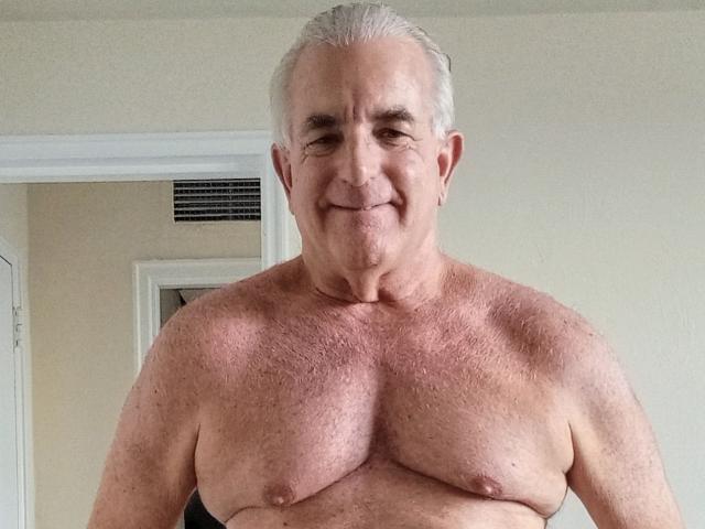 ShoreCock is an older, shirtless guy with gray hair, small tits, and a slight smile. He has a light skin tone and a bit of chest hair.
