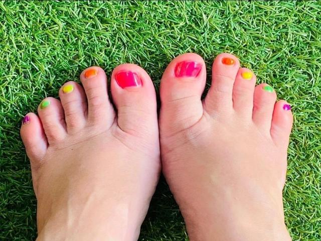 LiesaBDSM-hot's feet with colorful toenails: pink, yellow, orange, red, and purple on a green grassy surface.