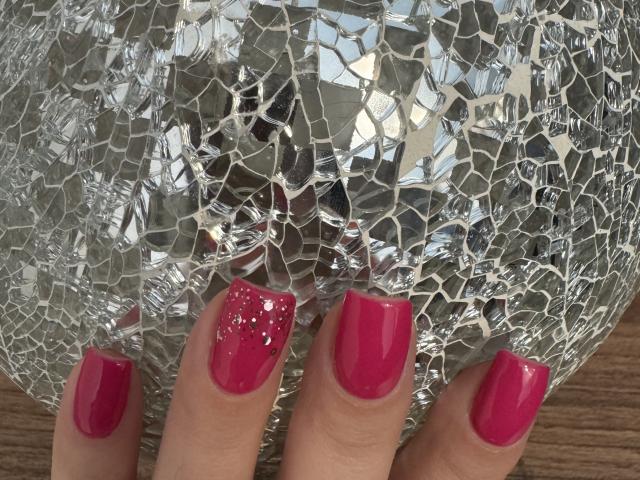 As unhas rosa de Lany Jolene, com glitter no dedo indicador, seguram uma bola de mosaico prateada e refletiva. Seus dedos estão ligeiramente curvados..