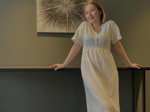 Sillitls with pale skin, short blonde hair, and small tits, wearing a white dress, leaning on a black railing, smiling. Art with black lines on gray wall behind.