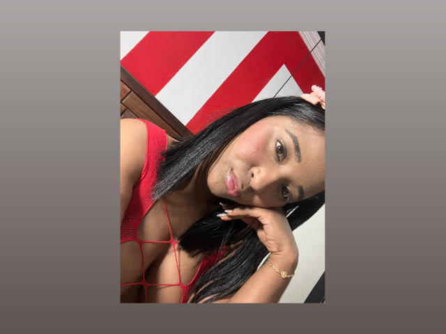 MelanyScoth with dark, straight hair, red string bikini, pouty lips, and pink hair clip, resting chin on hand, looking at camera, wearing gold bracelet, in bright light.