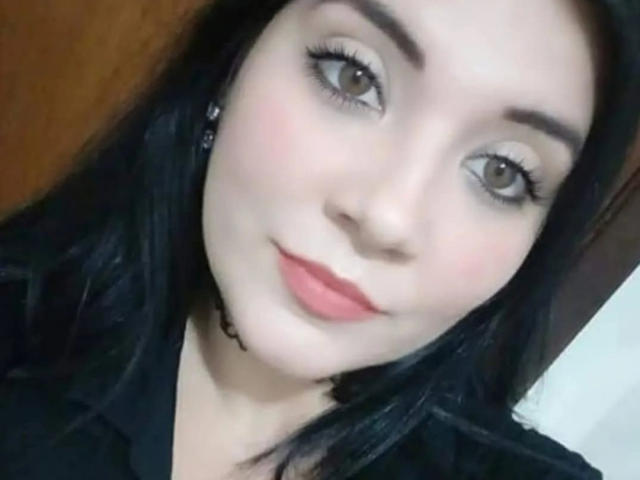 SafaDosDos has pale skin, black hair, green eyes, and pink lips with a slight smile. She's wearing black clothes and has a black choker. She looks cute and sexy.