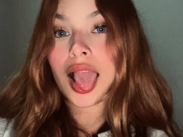 ShantalSummer ha i capelli castano chiaro, gli occhi azzurri e tiene la lingua fuori in modo giocoso. Le sue labbra rosa sono leggermente aperte, mostrando un po' della sua lingua. Il suo viso è centrato..