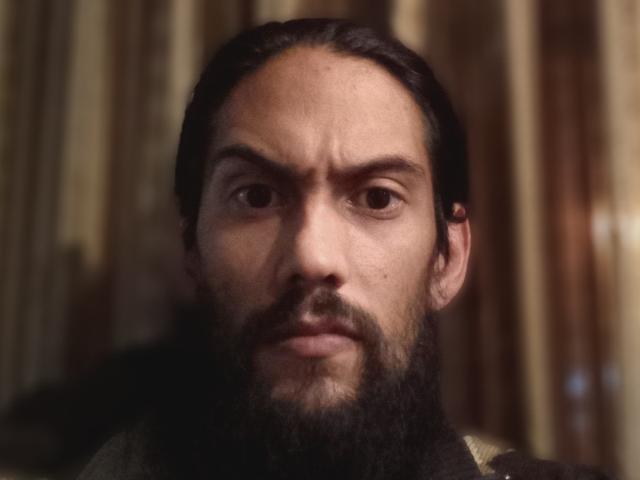 Morochoo69 has a serious face, dark beard, and slicked-back hair. His brown eyes and slightly furrowed brow give a determined look. He's wearing a dark, patterned garment.