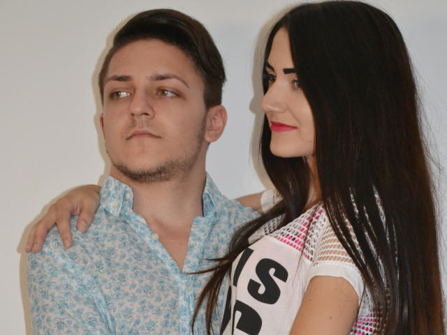 HotCoupleAnal, a dude with short brown hair and a light blue patterned shirt, has his arm around a HotCoupleAnal with long black hair, red lipstick, and a white shirt.
