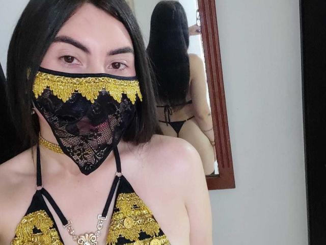 MorboErotico69 with black lace mask, yellow and black lace bra, and choker, showing off her tits in a mirror selfie, reflecting her ass. Long black hair, brown eyes.