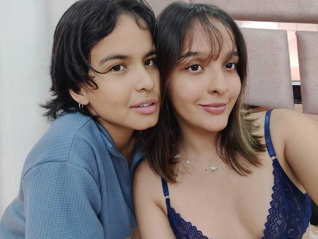 AnneAndSophia with short black hair in a blue shirt, and AnneAndSophia with brown hair in a blue lace bra, both smiling, showing small tits and a cute nose.