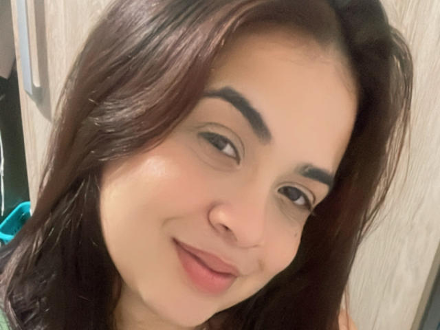 Beatrixzz has brown hair, dark eyebrows, light skin, and a small smile with pink lips. Her brown eyes are slightly squinted. She's looking at the camera.
