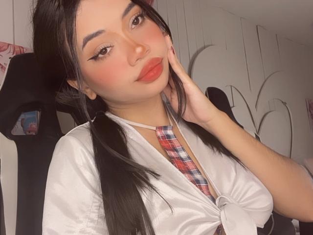LiliMays has puffy red lips, black pigtails, and wears a tied white shirt with a plaid necktie, hand on cheek, looking at camera, soft lighting, cute.