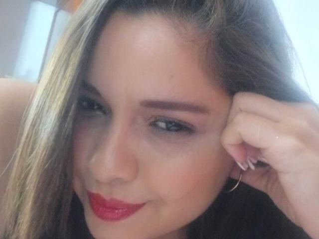 IdyllaJhones ha i capelli castano chiaro, rossetto rosso e un leggero sorriso, con la mano vicino all'orecchio. Indossa un orecchino a cerchio dorato e ha sopracciglia ben definite..