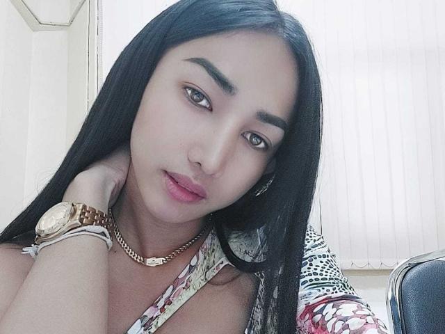 Sofinaughty69 has long black hair, brown eyes, and pink lips. She's wearing a floral dress, a gold watch, and a chain necklace, looking sexy with her hand on her neck.