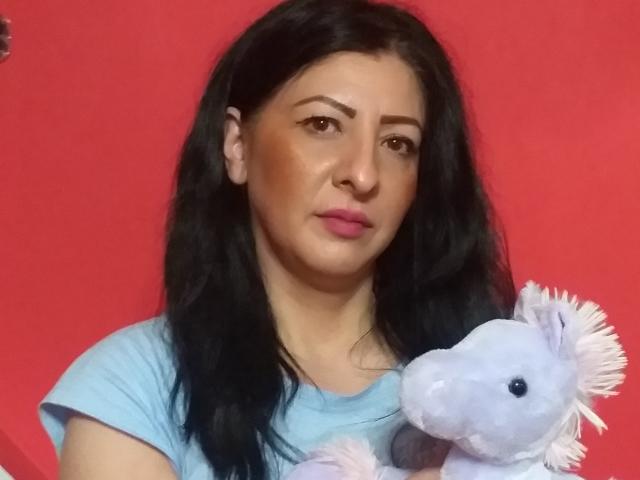 Alinnes with black hair, pink lipstick, and light blue shirt, holding a purple stuffed horse with white mane, against a red background.