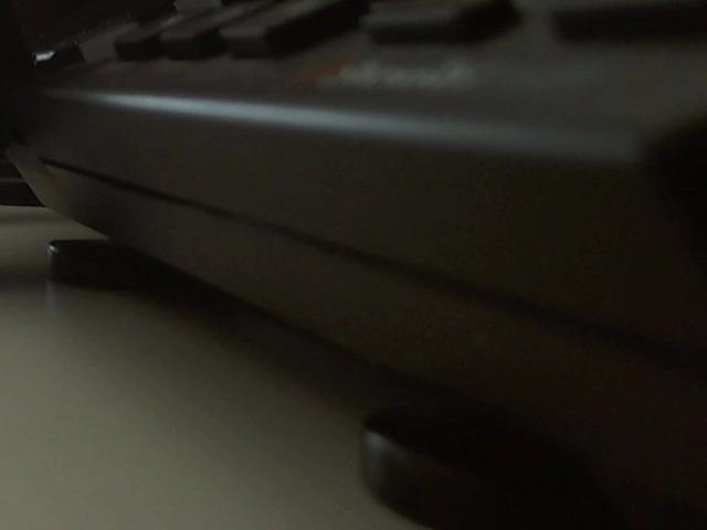 Black keyboard, slightly blurry, with dark keys and a visible keycap in the bottom right, lying on a flat surface, close-up shot. FlipFlops-hot's ass, barely visible.