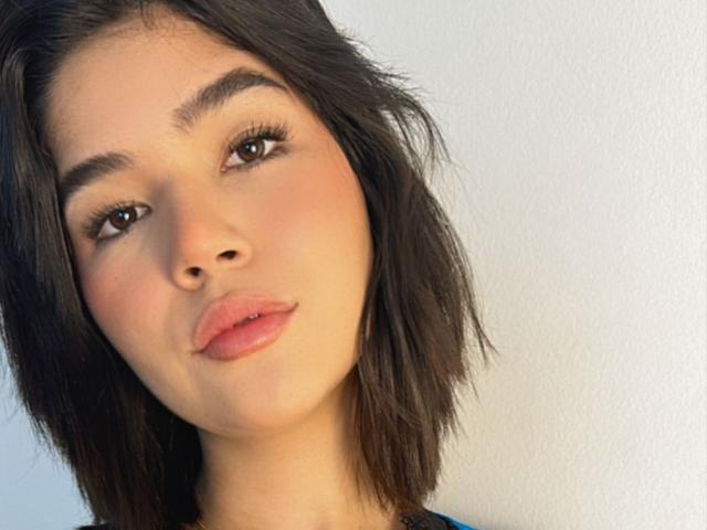 ScarlletZhen has brown eyes, full pink lips, and medium-length dark brown hair, looking slightly to the side with a subtle, confident expression. Her skin is fair and smooth.