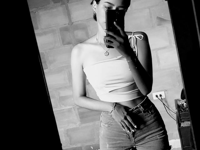Black-and-white selfie of CaterinaRomano with a slim build, small tits, wearing a strapless top and high-waisted jeans, holding a phone, in front of a mirror.