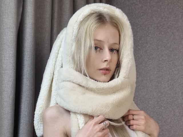 ExcitedBlizzard with pale skin, blonde hair, and freckles, wrapped in a fluffy white towel, holding it over her tits, looking at the camera with a neutral expression.