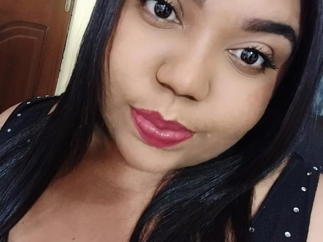 SarahSmity's face, showing her brown eyes, pink lipstick, and black hair, wearing a black polka-dotted top, with a cute, slightly pouty expression.