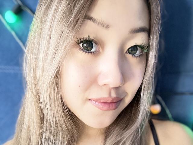 RenyLime has light brown hair, green eyes, long lashes, and a slight smile. She's looking at the camera with a cute, innocent expression. Boobs are not visible.