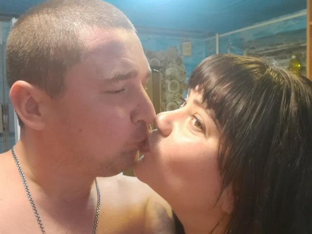 DebbieXRoy with short brown hair and DebbieXRoy with a shaved head, kissing. DebbieXRoy's nose is touching DebbieXRoy's nose. DebbieXRoy wears a necklace, DebbieXRoy is topless.