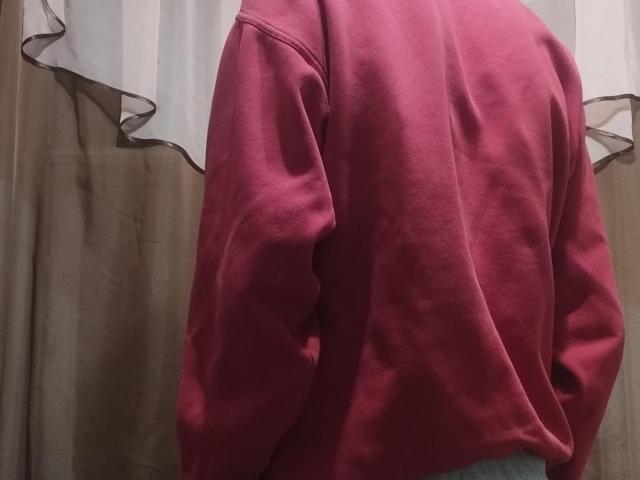 Le pull rose de WinterBrian, qui couvre les fesses, avec de longues manches, légèrement ample et lâche, se tient devant des rideaux beige et blancs. Aucune autre partie ou détail visible..