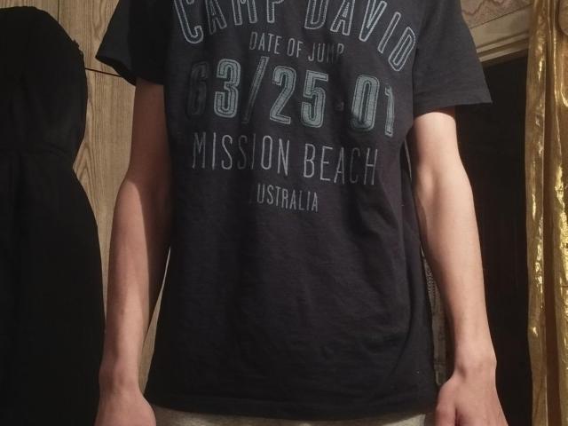 WinterBrian's bare arms and a dark gray T-shirt with "3/25/01" and "Mission Beach, Australia" text. No pants visible. Shitload of muscle tone.