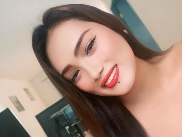 AlwinaForU with long brown hair, red lipstick, and a nose piercing, smiling with a lip piercing, showing off her cute face and smooth skin.