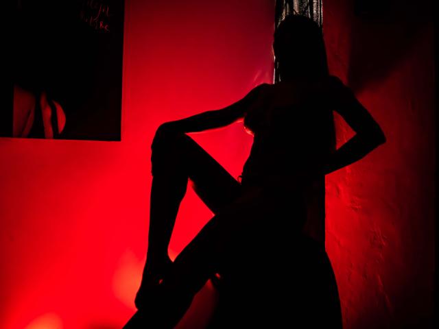 Silhouette von Rosalinda Cortez, ein Bein angehoben, Hände an der Hüfte, rotes Licht betont ihren Körper, sichtbare Brüste und Gesäß, in einem dunklen, stimmungsvollen Foto..