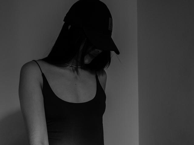 EuphoriaRush in een zwarte tanktop, met een baseballpet op, hoofd naar beneden, kleine borsten, slank, lichtgetint, donker haar, foto in grijstinten met schaduwen..