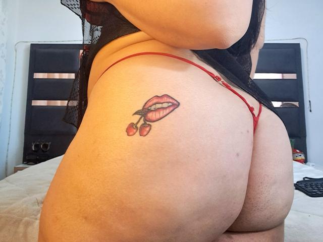VivianaThomson's butt tattoo of red lips with a cherry, wearing a red thong and black lace top, showing her curvy, pale-skinned, buttcheek.