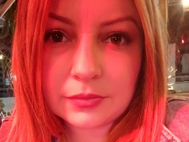 NatalyHami has red-orange hair, brown eyes, and pink lips. Her nose is slightly upturned. Her eyebrows are thin. Her skin is fair with a slight red glow.