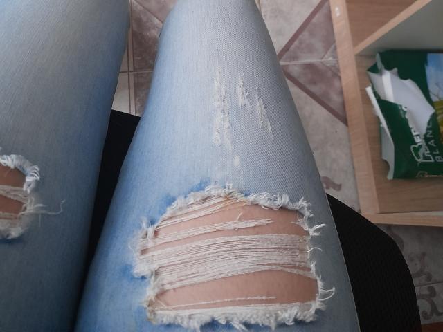 KatherinGrey's ripped blue jeans with frayed white edges showing her pale skin, sitting with her legs crossed, showing a large tear on the upper thigh.