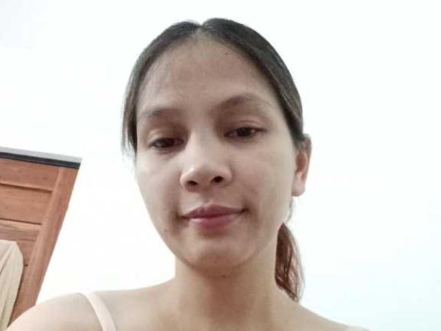 HotSexyTits with light brown skin, small nose, brown eyes, dark brown hair in a ponytail, smiling slightly, wearing a pink tank top, no visible boobs or ass.