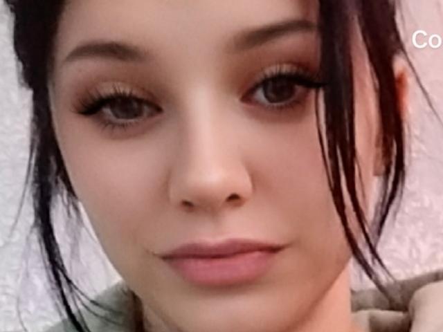 El rostro de ShellyLili, con sus ojos marrón oscuro, sus largas pestañas negras y sus labios rosados, sus cejas marrones ligeramente levantadas, y su cabello negro que cubre parcialmente sus orejas. Piel suave y clara..