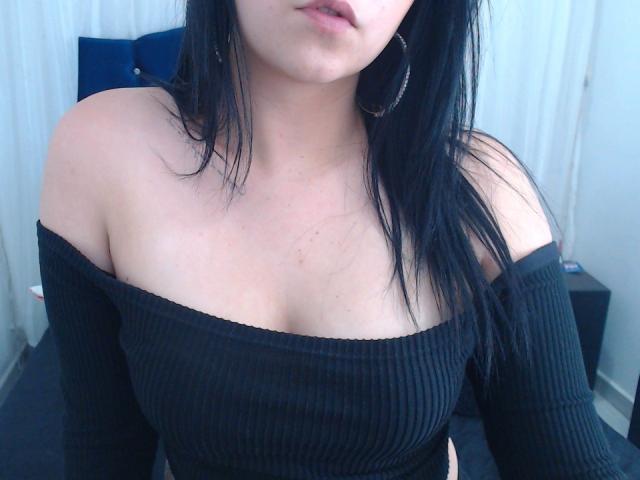 Kkatalina with black ribbed off-shoulder top, showing her bare shoulders and upper chest. She has black hair, hoop earrings, and a slight tan. Boobs visible, nipples not.