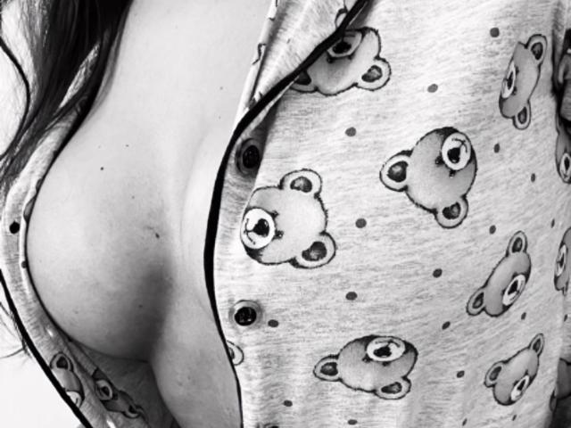 GatinhaCarinhosa's side boob in a grey, teddy bear-patterned shirt, partially open, revealing a bit of her soft, fair-skinned chest and long, dark hair.