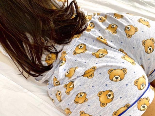 GatinhaCarinhosa's ass is covered in a gray, teddy bear print pajama set, lying on a white bed with brown, wavy hair partially covering the upper back.