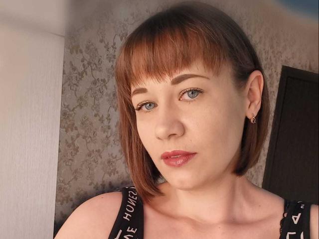 MarlynMartie has short brown hair, blue eyes, and pink lipstick. She's wearing black straps with "HOLLYWOOD" in white. She's also got a small earring in her right ear.