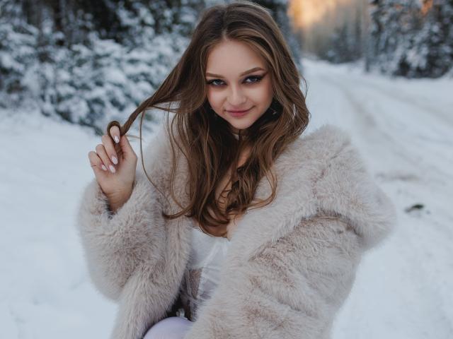MayxFlower with long brown hair, wearing a fluffy beige fur coat, holding her hair, smiling, in a snowy forest, showing her tits slightly through the coat.