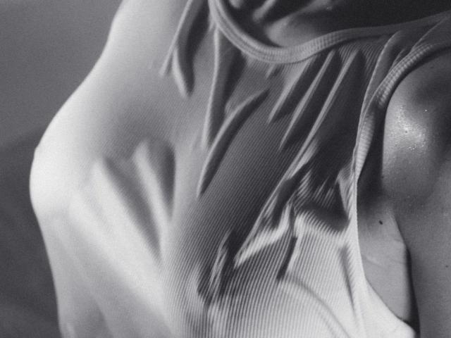 Black-and-white photo of LisaMetalHoney's chest in a ribbed tank top, showing her small, perky tits and a shiny, sweaty shoulder. Focus on her upper body.