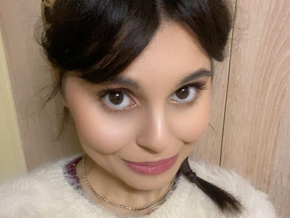 MeEleonora has medium brown eyes, dark brown hair in a braid, pink lipstick, and a cute smile, wearing a fluffy white top with a gold chain necklace.