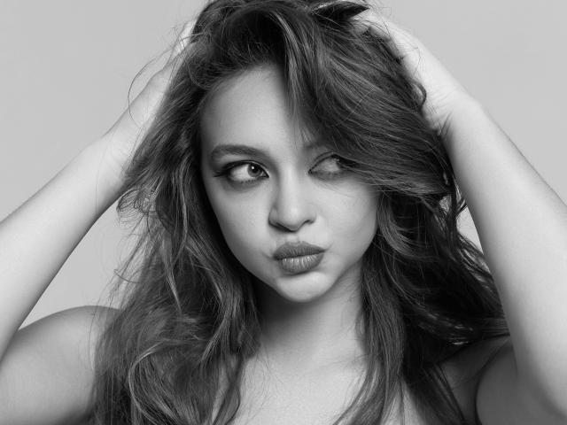 Black-and-white photo of MayxFlower with messy, wavy hair, hands in hair, winking, pouty lips, and a sexy, confident expression, showing her tits and cute face.