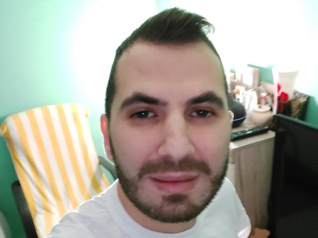 EnddyHottx has a short, dark brown, slightly messy haircut with a beard, light skin, and is wearing a white shirt, looking at the camera with a subtle smile.