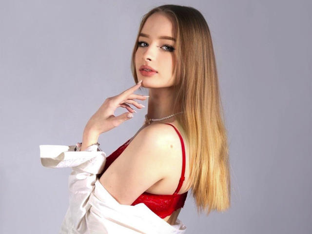 LilaFantasy avec de longs cheveux blonds, un soutien-gorge en dentelle rouge, une chemise blanche portée par-dessus les épaules, un doigt sur la lèvre, un collier de perles, regardant en arrière, sexy, mignonne, peau pâle, maquillage discret, expression douce..
