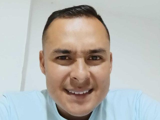 AmorDeDos69 has a chubby face, short black hair, and is smiling with a light skin tone, wearing a light blue shirt, brown eyes, and a slight nose tan.
