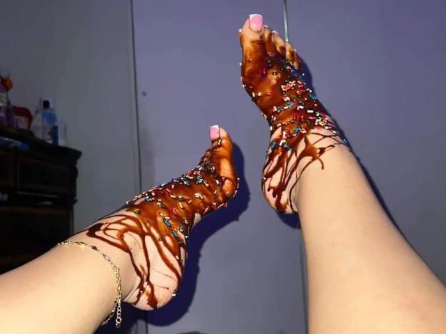 TerryBenson's feet covered in chocolate and colorful sprinkles, with pink toenails, a gold anklet, and a slight ankle bracelet, in a provocative and playful pose.